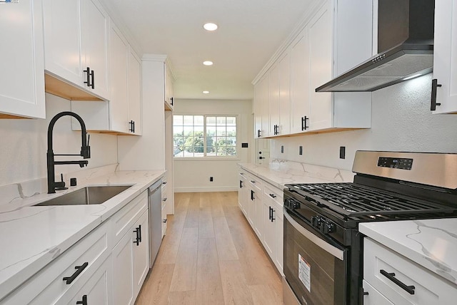 kitchen with wall chimney exhaust hood, sink, white cabinetry, light stone counters, and stainless steel appliances