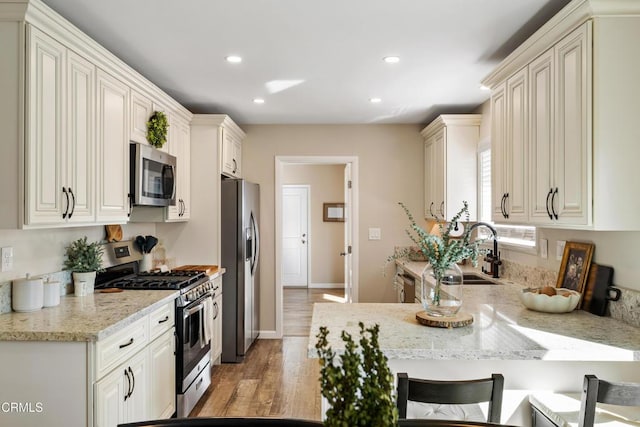 kitchen with a kitchen bar, sink, light stone counters, stainless steel appliances, and light hardwood / wood-style floors