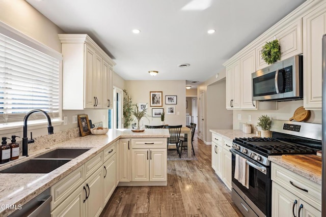 kitchen with light stone counters, stainless steel appliances, sink, and light wood-type flooring