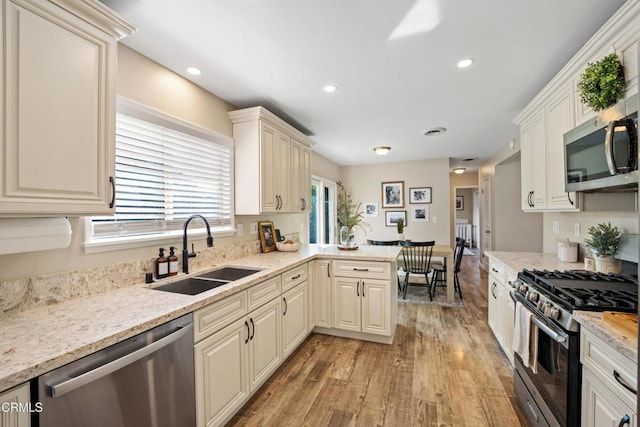 kitchen featuring appliances with stainless steel finishes, kitchen peninsula, sink, light stone counters, and light hardwood / wood-style floors