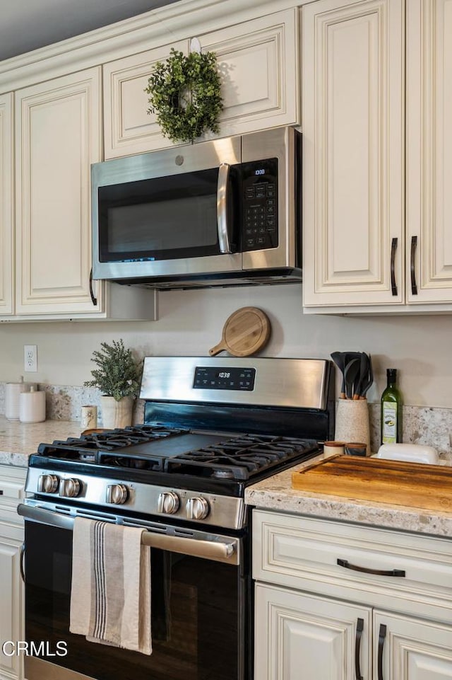 kitchen with light stone counters, cream cabinets, and stainless steel appliances