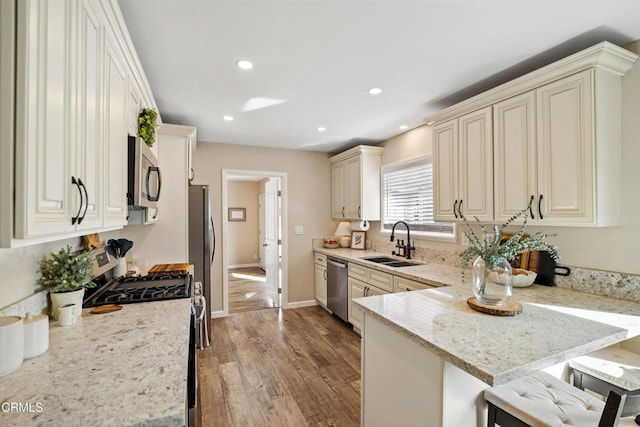 kitchen featuring sink, a breakfast bar area, appliances with stainless steel finishes, kitchen peninsula, and light stone countertops