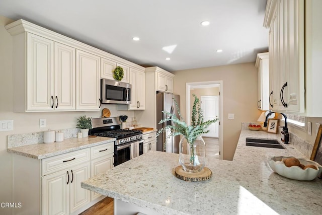 kitchen with stainless steel appliances, light stone countertops, sink, and kitchen peninsula