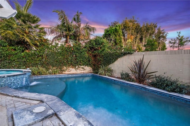 pool at dusk featuring an in ground hot tub