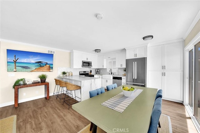 dining space with crown molding, sink, and light wood-type flooring