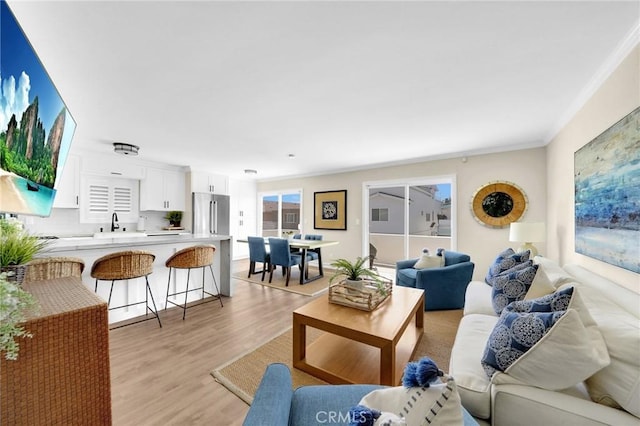 living room featuring crown molding, sink, and light hardwood / wood-style flooring