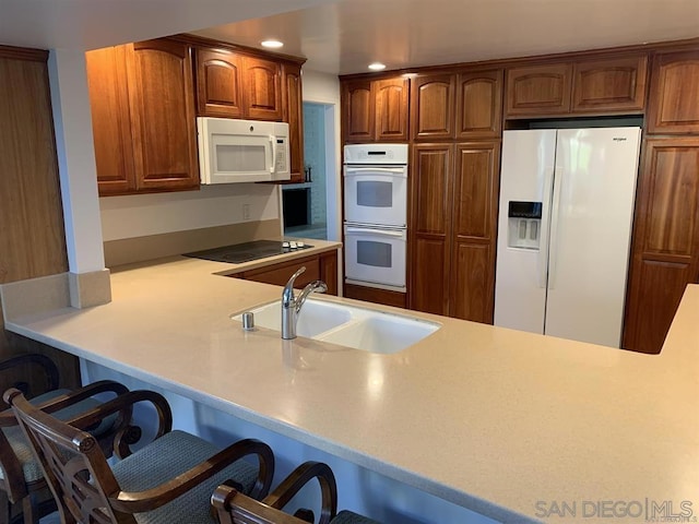 kitchen with sink, white appliances, a breakfast bar area, and kitchen peninsula