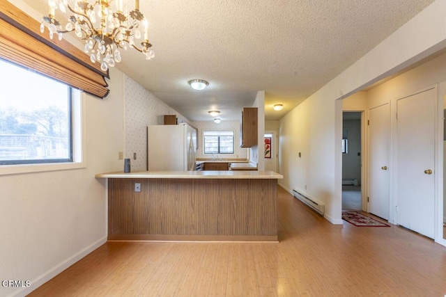 kitchen with a baseboard radiator, white fridge, light wood-type flooring, and kitchen peninsula