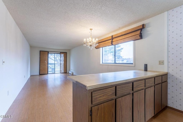 kitchen with a healthy amount of sunlight, kitchen peninsula, a textured ceiling, and light wood-type flooring