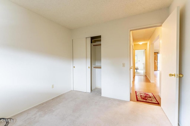 unfurnished bedroom with light carpet, a textured ceiling, and a closet