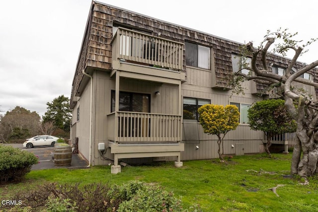 rear view of house featuring mansard roof and a lawn
