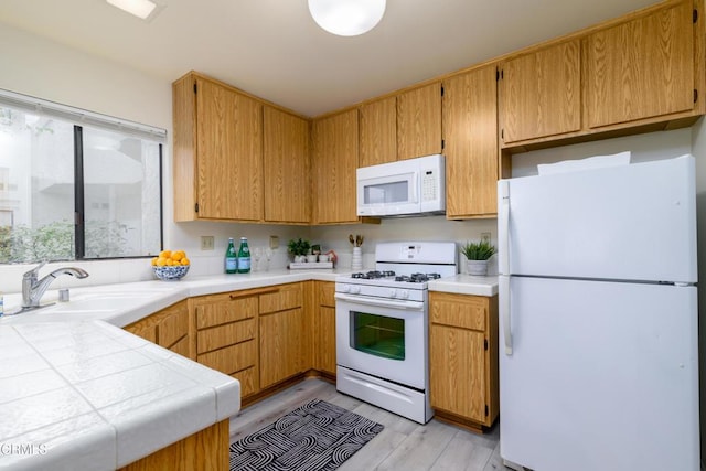 kitchen with white appliances, tile counters, sink, and light hardwood / wood-style flooring