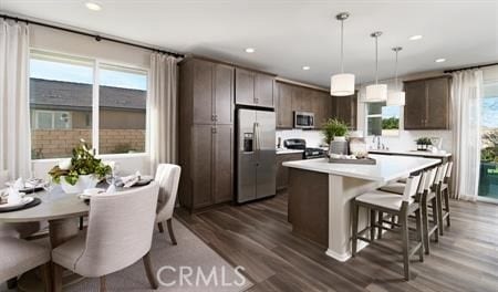 kitchen featuring a kitchen island, appliances with stainless steel finishes, decorative light fixtures, dark brown cabinetry, and a healthy amount of sunlight