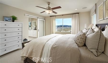 carpeted bedroom with a barn door and ceiling fan