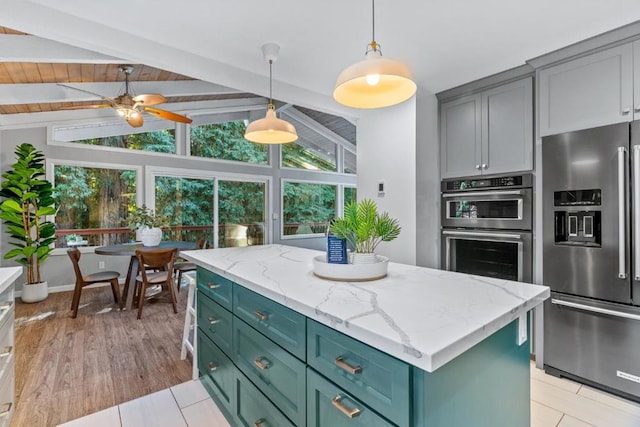 kitchen with a wealth of natural light, vaulted ceiling with beams, a center island, stainless steel appliances, and light stone countertops