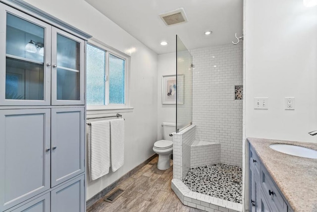 bathroom featuring vanity, toilet, wood-type flooring, and a tile shower