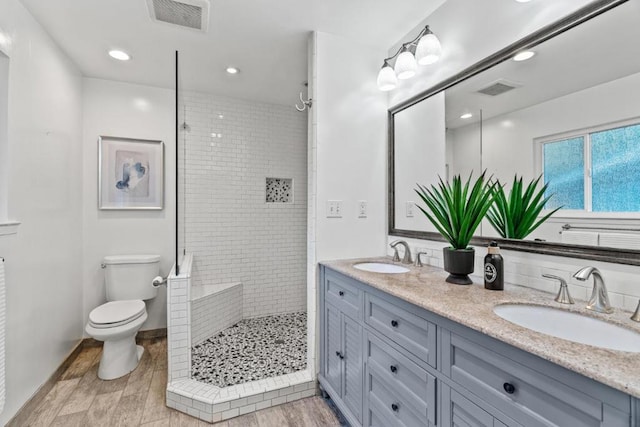 bathroom with hardwood / wood-style flooring, vanity, toilet, and a tile shower