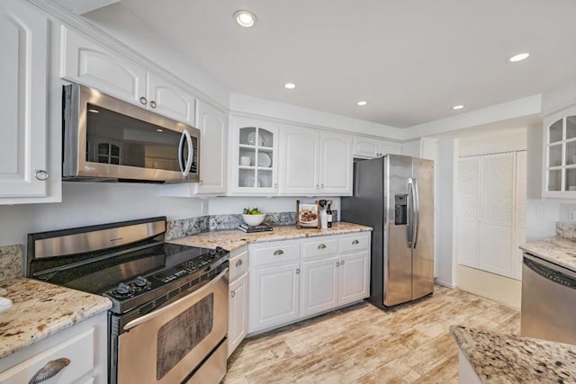 kitchen with light stone countertops, white cabinetry, appliances with stainless steel finishes, and light hardwood / wood-style floors