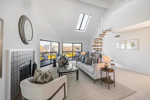 carpeted living room featuring a tile fireplace, high vaulted ceiling, and a skylight