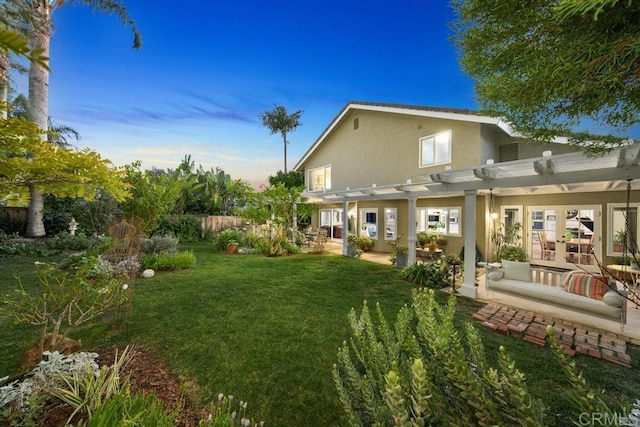 back house at dusk with a patio, a pergola, and a lawn