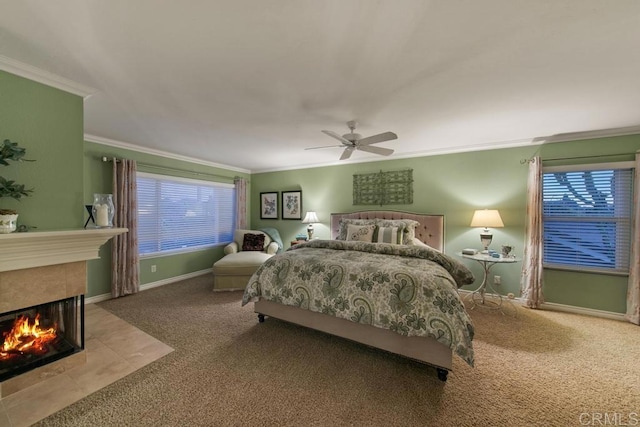 bedroom featuring a tiled fireplace, crown molding, carpet floors, and ceiling fan