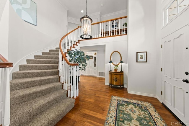 foyer entrance featuring crown molding, dark wood-type flooring, a notable chandelier, and a towering ceiling