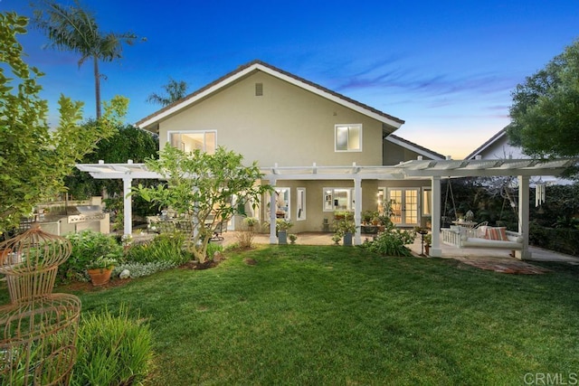 back house at dusk with a yard, a pergola, a patio area, and exterior kitchen