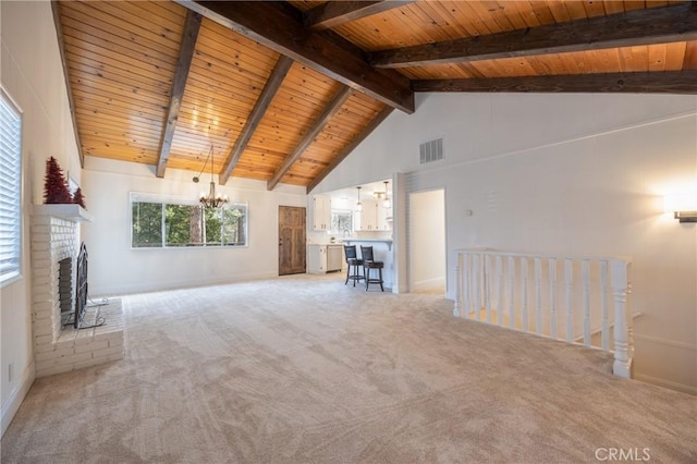 unfurnished living room featuring beamed ceiling, a chandelier, wood ceiling, a brick fireplace, and light carpet