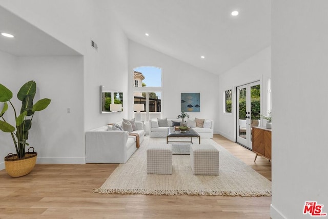 living room with light hardwood / wood-style flooring, high vaulted ceiling, and french doors