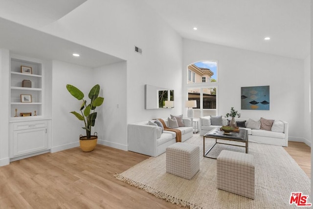 living room with high vaulted ceiling, built in features, and light hardwood / wood-style floors