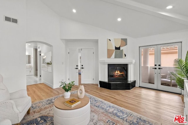 living room featuring french doors, high vaulted ceiling, a tile fireplace, and light hardwood / wood-style flooring