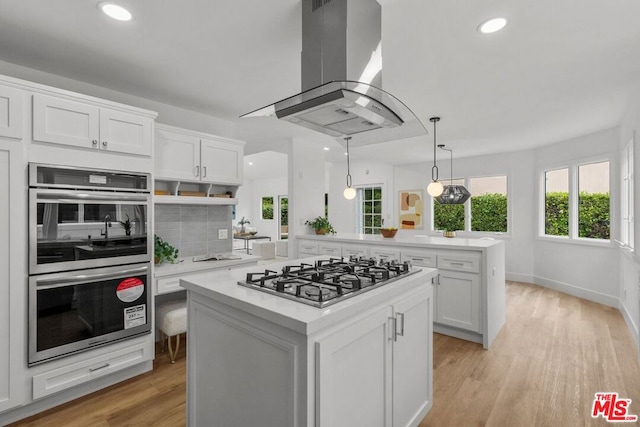 kitchen with white cabinetry, island exhaust hood, appliances with stainless steel finishes, and kitchen peninsula