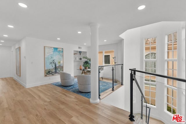 hall featuring built in shelves, light hardwood / wood-style flooring, and ornate columns