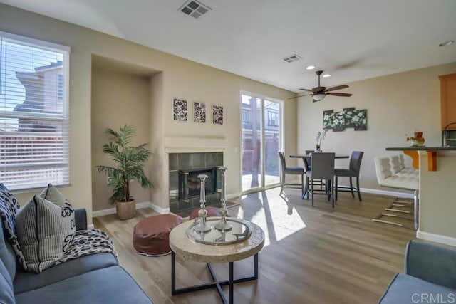 living room featuring a tile fireplace, ceiling fan, and light hardwood / wood-style flooring