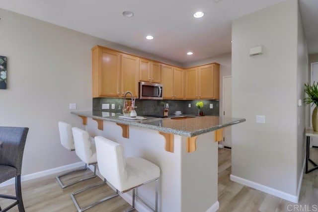 kitchen with backsplash, light brown cabinets, kitchen peninsula, and a kitchen bar