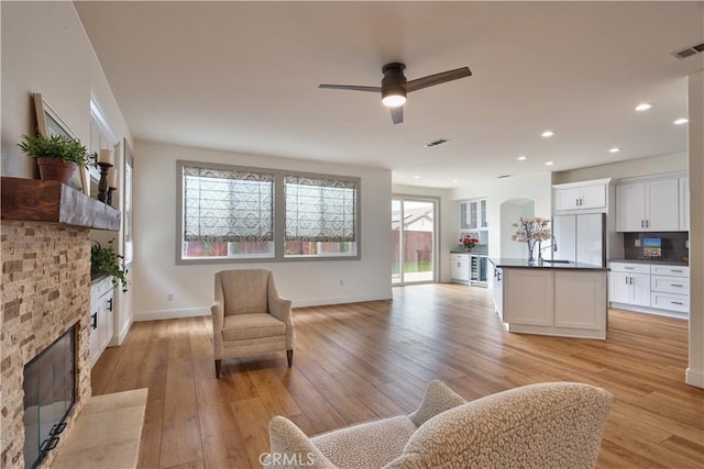 living room featuring sink, a stone fireplace, light hardwood / wood-style floors, and ceiling fan