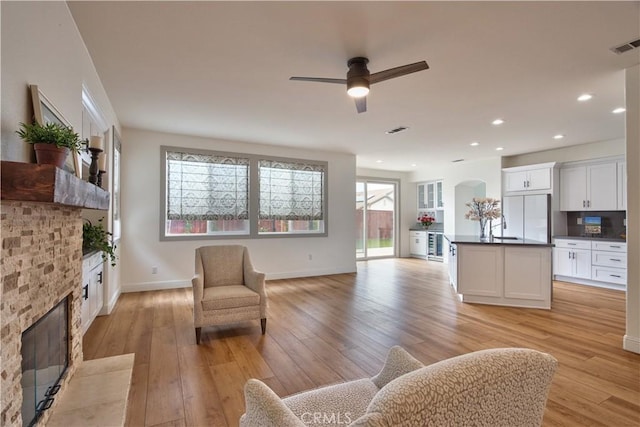 living room with a stone fireplace, light wood-style flooring, recessed lighting, visible vents, and baseboards