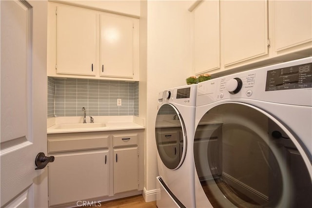 clothes washing area with sink, washing machine and dryer, cabinets, and light wood-type flooring