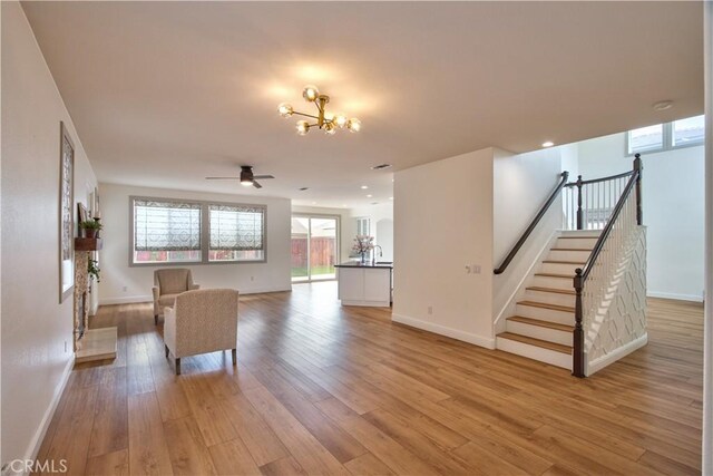 unfurnished living room featuring ceiling fan with notable chandelier and light hardwood / wood-style floors