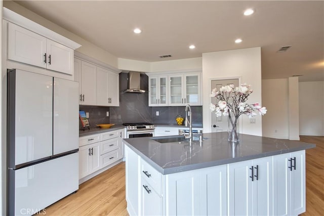 kitchen featuring white cabinetry, wall chimney exhaust hood, white fridge, and a center island with sink