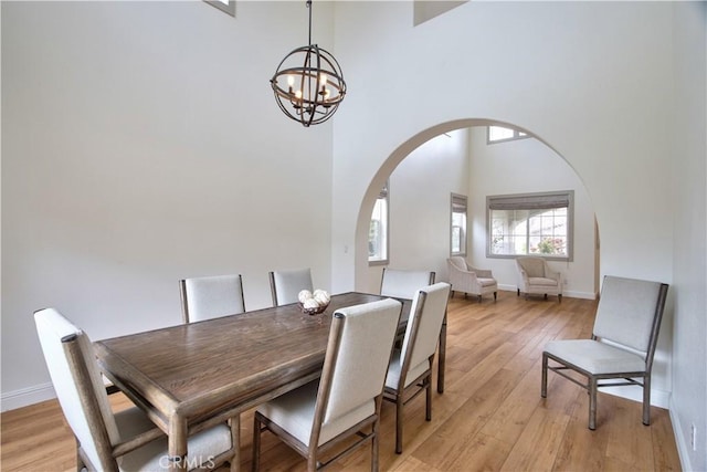 dining room featuring a notable chandelier, a towering ceiling, and light wood-type flooring