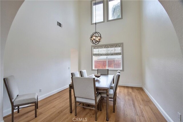 dining space featuring a notable chandelier, a towering ceiling, and light hardwood / wood-style floors