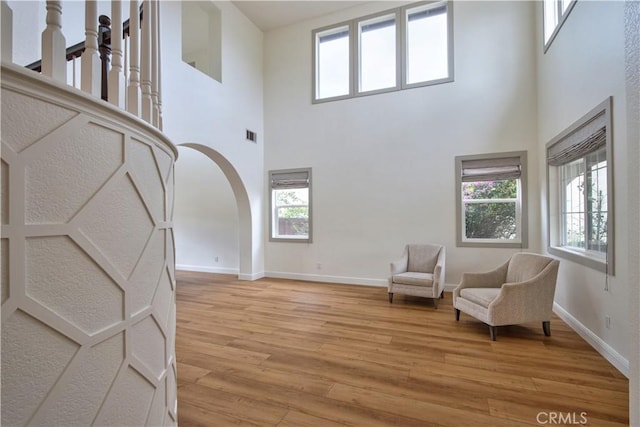 living area with a wealth of natural light, arched walkways, baseboards, and light wood-style floors