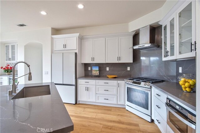 kitchen with appliances with stainless steel finishes, sink, white cabinets, and wall chimney exhaust hood