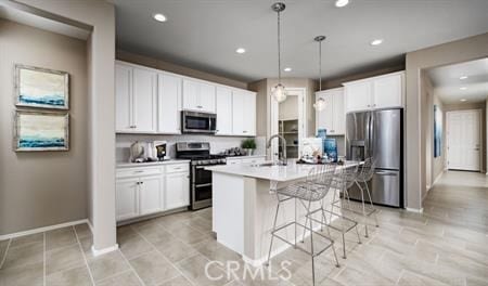 kitchen featuring stainless steel appliances, an island with sink, pendant lighting, and white cabinetry