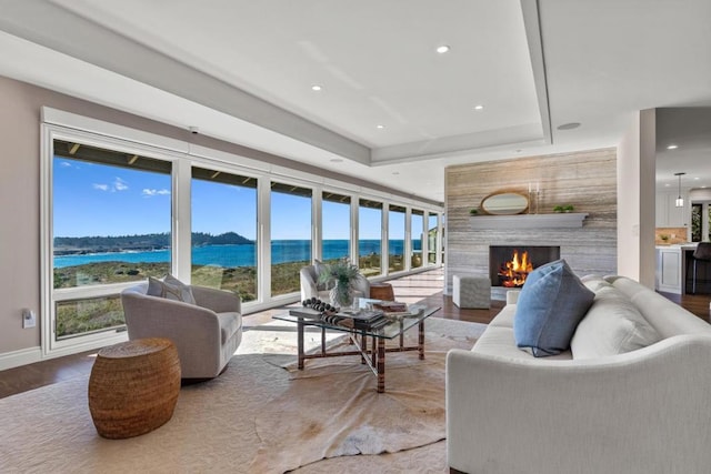 living room featuring a water view, a high end fireplace, a tray ceiling, and hardwood / wood-style floors