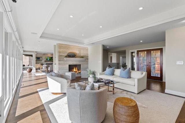 living room featuring a raised ceiling, a large fireplace, light hardwood / wood-style floors, and french doors