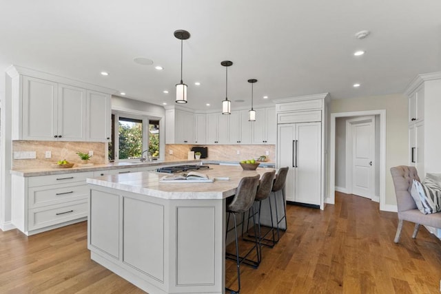 kitchen with a breakfast bar, white cabinetry, decorative light fixtures, paneled built in refrigerator, and a kitchen island