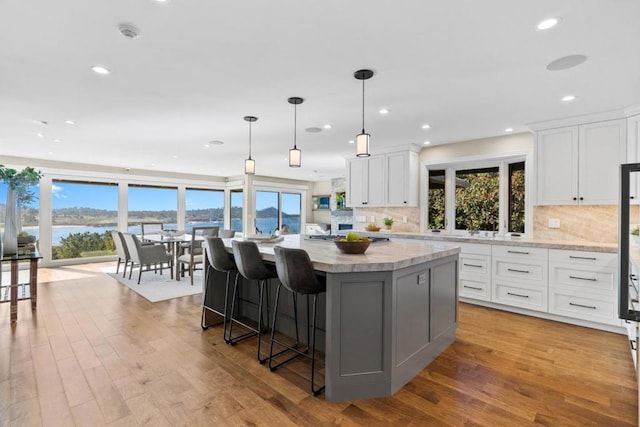 kitchen with white cabinetry, a kitchen breakfast bar, a center island, a water view, and decorative light fixtures