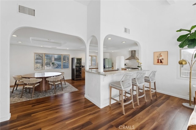 kitchen featuring a breakfast bar, tasteful backsplash, dark hardwood / wood-style flooring, kitchen peninsula, and wall chimney exhaust hood